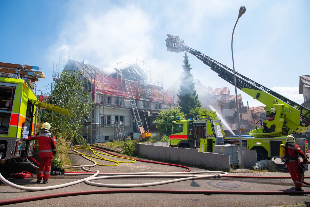 Eine Drehleiter und Feuerwehrleute stehen vor einem brennenden Gebäude in Adetswil.